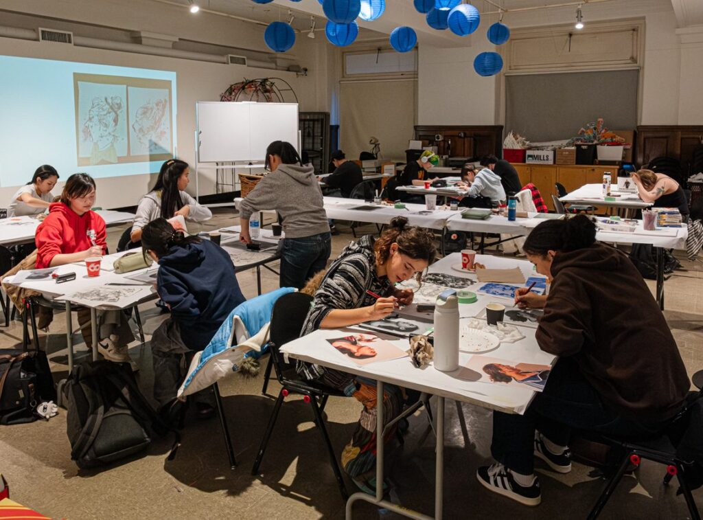 A room of teenagers create art at different tables.
