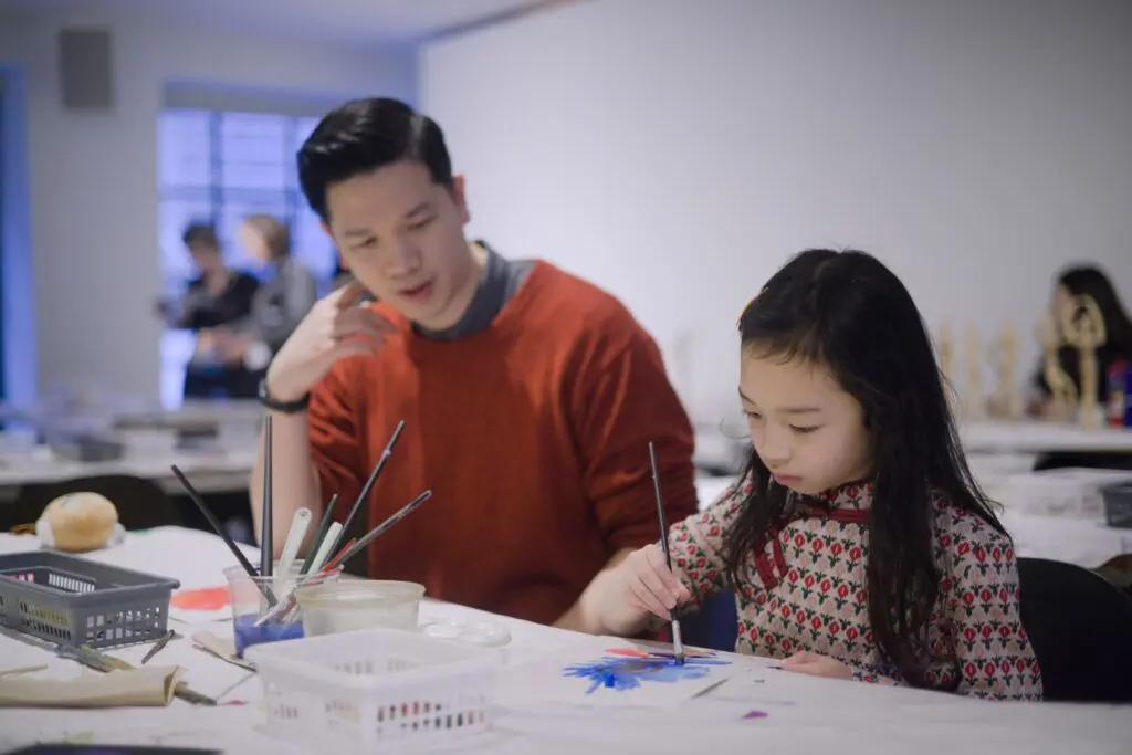 A father and daughter sitting at a table painting.