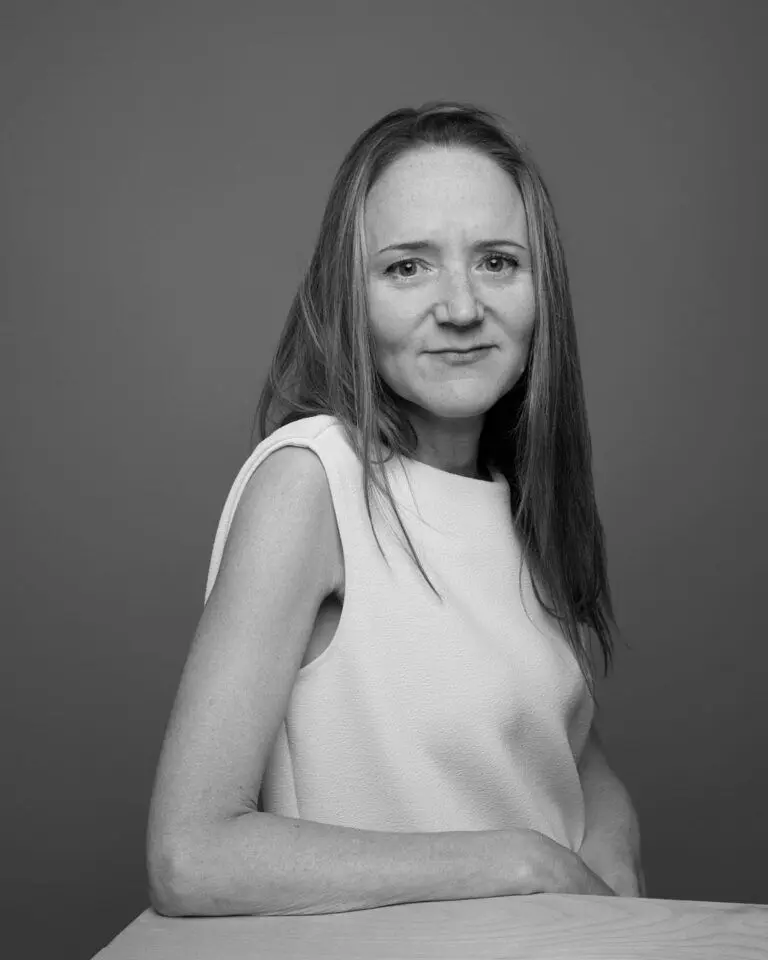 Woman in white shirt with blond hair looks out at the camera