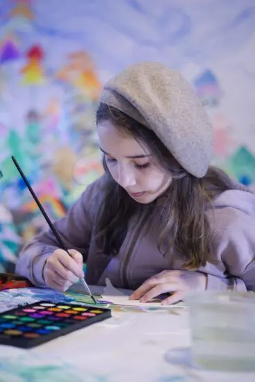 A young girl sitting at a table painting with watercolours.