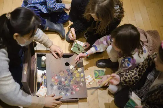 An Art Educator demonstrates painting for four children using a palette covered in paint.
