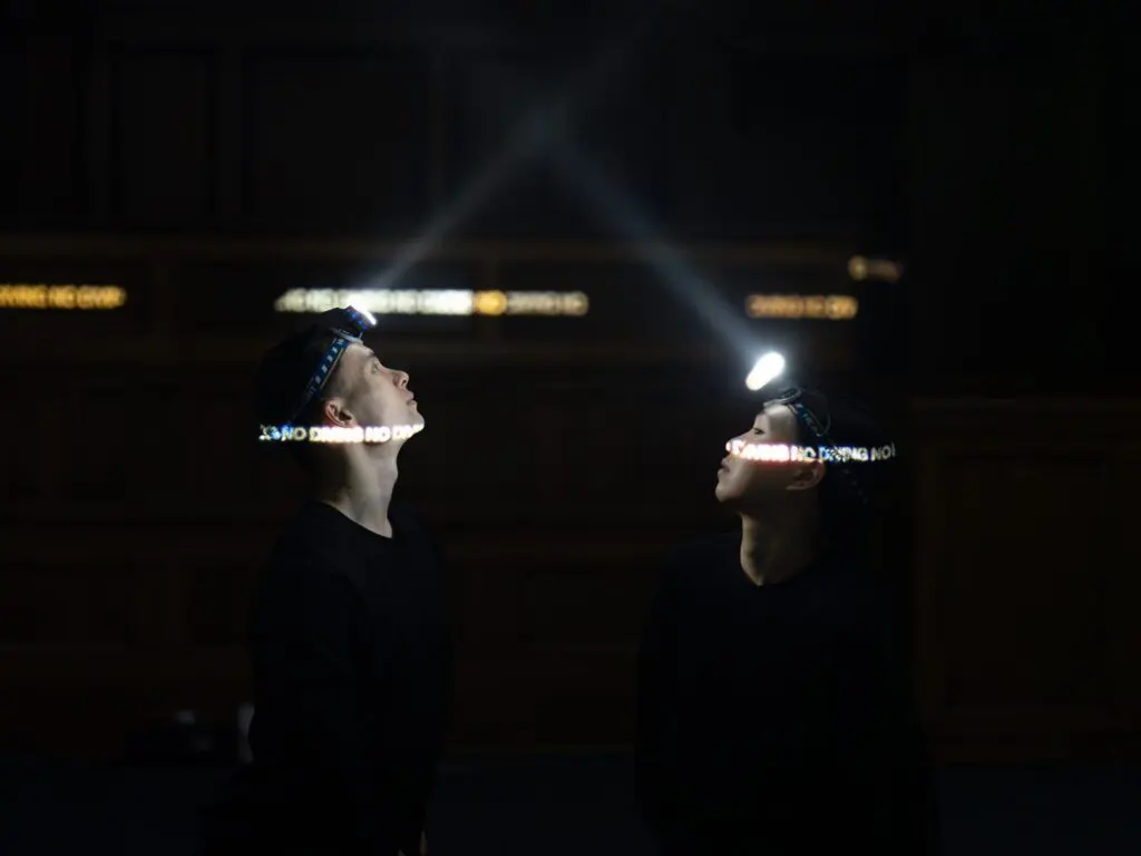 Two performers standing face-to-face wearing headlamps.