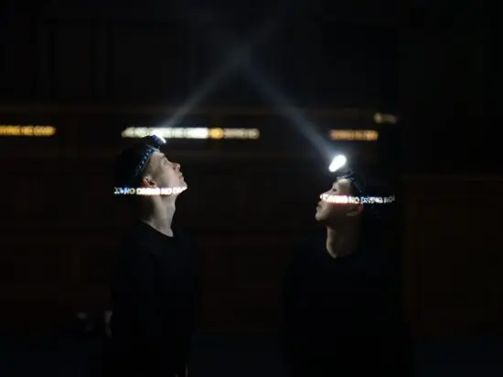 Two performers standing face-to-face wearing headlamps.