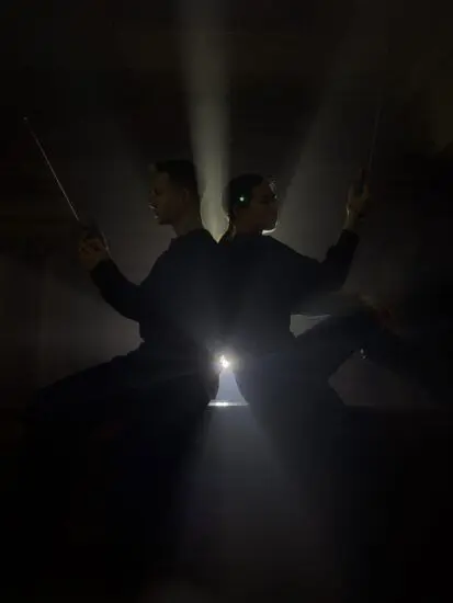 Two performers sitting back-to-back and holding handheld radios, in front of a spotlight.