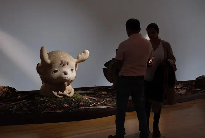 Two people, a man and a woman, look at Otani Workshop's large-scale ceramic sculpture of a moose.