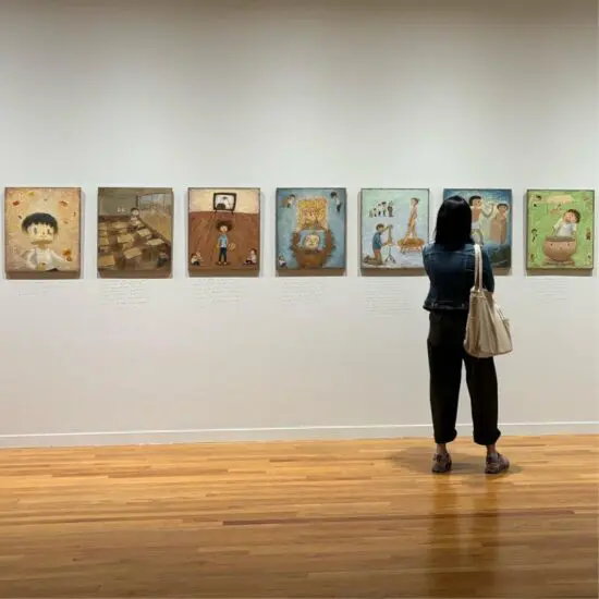 Visitor looking at paintings by artist Otani Workshop hung in a long row.
