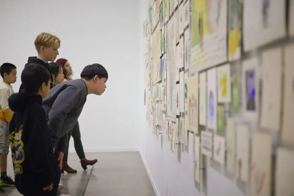 A group of students seen from the side looking at artwork on the wall.